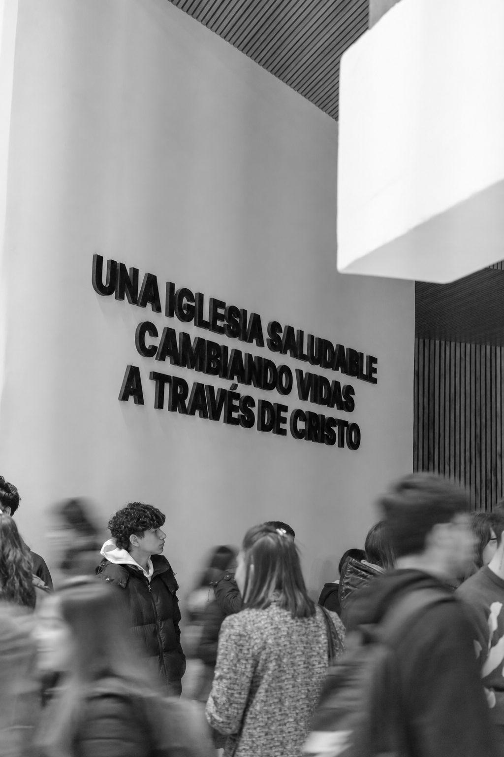 Personas en el hall de la iglesia, junto al mensaje Una iglesia saludable cambiando vidas a través de Cristo